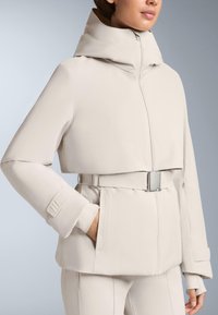 Svjetlobež jakna s visokim ovratnikom, dugim rukavima i pojasom u struku. Ima zatvaranje na patentni zatvarač i teksturiranu tkaninu s glatkim finišem.