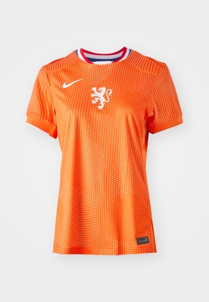 Orange Fußballtrikot mit weißem Löwenemblem, Rundhalsausschnitt mit roten und blauen Akzenten, gepunktete Oberfläche, kurze Ärmel und schwarzes Etikett.