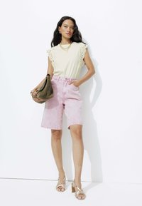 Haut beige clair avec des accents en dentelle, associé à un short en denim rose clair. Les accessoires comprennent des bijoux en or et un sac à main vert. Talons beiges.