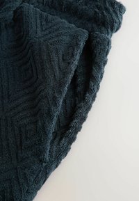 Toalla azul oscuro, de textura suave, con un patrón geométrico. Los bordes están ligeramente deshilachados, mostrando la suavidad y capacidad de absorción de la toalla.