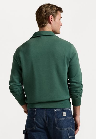 Pullover in maglia verde con colletto, polsini e orlo a costine. La vista posteriore mostra una texture liscia e una vestibilità rilassata, abbinato a pantaloni in denim.