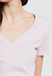 Světle růžové tričko s výstřihem do V, krátké rukávy, měkký bavlněný materiál, hladká textura, minimální švy, těsný výstřih.