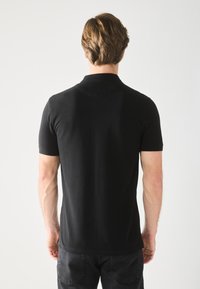 Sort polo-skjorte med korte ærmer og en krave, lavet af glat stof. Har en lige pasform og minimal syning detaljer.