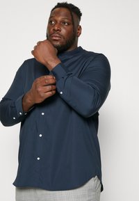 Navy blue long-sleeve shirt with a mandarin collar, button-down front, and smooth, textured fabric. Features cuff button details.