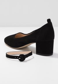 Chaussure à talon bloc en daim noir avec bout arrondi, présentée avec une bride de cheville amovible assortie dotée d'une boucle circulaire.