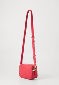 Sac bandoulière rectangulaire rouge en matériau synthétique texturé. Il dispose d'une bandoulière réglable et d'accents en métal doré.