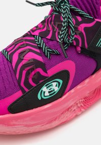 Lilla atletisk sko med en struktureret overdel, dristige pink accenter, sorte detaljer, mønstrede snørebånd og et markant brandlogo på siden.