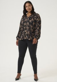 Sort blomsterbluse med lange ærmer, der har pink og gule blomsterdesigns, parret med sorte skinny jeans og sorte stilethælssko.