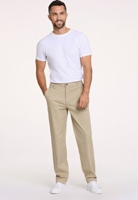 Beżowe chinosy z płaskim przodem, kieszeniami bocznymi i zapięciem na guzik. Połączone z gładką białą koszulką i białymi trampkami.