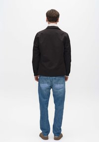 Schwarze Jacke mit Kragen, getragen über einem weißen Hemd, kombiniert mit blauen Denim-Jeans mit hellblauen Taschenakzenten.