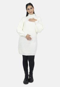 Cremefarvet strikket kjole med høj hals, ribbet struktur og ballonærmer, parret med sorte leggings og snørebåndsstøvler.