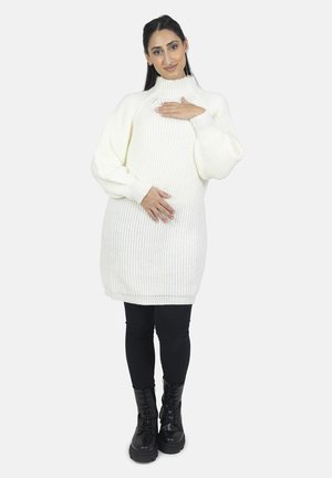 Cremefarvet strikket kjole med høj hals, ribbet struktur og ballonærmer, parret med sorte leggings og snørebåndsstøvler.