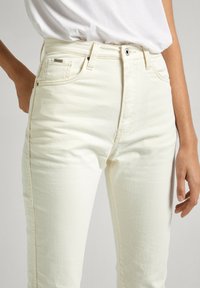 Jeans in denim bianco con una vestibilità slim. Presentano tasche frontali, cuciture leggere e un tag del marchio discreto sulla vita. Texture liscia.