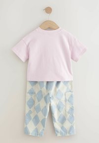 Camiseta de algodón rosa de manga corta, combinada con pantalones de color claro que presentan un patrón de diamantes azules y dos bolsillos laterales.