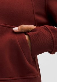 Felpa bordeaux con polsini a costine e tasca frontale, realizzata in un morbido tessuto testurizzato e con dettagli di cucitura visibili.