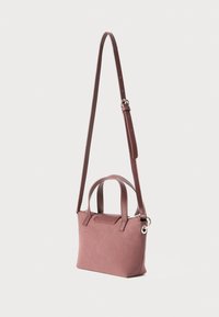 Small dusty pink handbag with suede texture, two short handles, and a long adjustable shoulder strap against a plain background.
