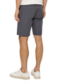 Dunkelgraue Baumwollshorts mit einer lässigen Passform, flachem Bund und Seitentaschen; getragen mit weißen Turnschuhen. Einfaches Design und weiche Textur.