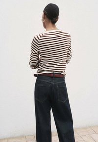 Gestreiftes langärmliges Oberteil in Braun und Creme, kombiniert mit dunkelblauen, weiten Jeans, versehen mit einem braunen Gürtel und einer glatten, strukturierten Oberfläche.