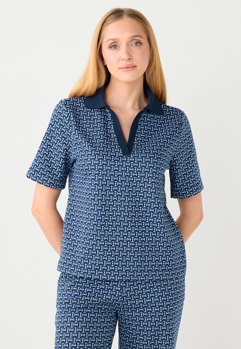 Polo bleu marine à manches courtes, avec un motif géométrique blanc et un col bleu marine uni. Le matériau a une texture lisse.
