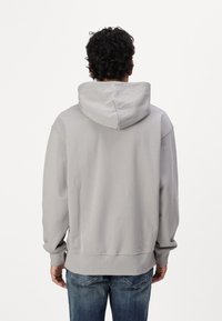 Helles graues Kapuzensweatshirt mit lockerer Passform, gerippten Bündchen und Saum, weichem Stoffgefühl, getragen mit blauen Jeans.