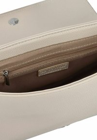 Interior de un bolso de cuero color beige claro con un bolsillo con cremallera, textura suave y un acento con un patrón sutil. Cierre a presión de plata visible.