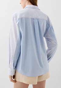 Lichtblauwe gestreepte button-up blouse met lange mouwen, een klassieke kraag en een plooien op de rug. De stof lijkt zacht met een gladde textuur.