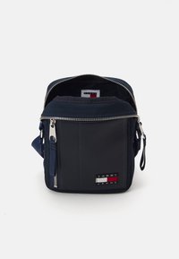 Bolso de bandolera navy hecho de nylon con cierre de cremallera, que presenta una tela texturizada, un parche con el logo en la parte delantera y un bolsillo lateral con cremallera.