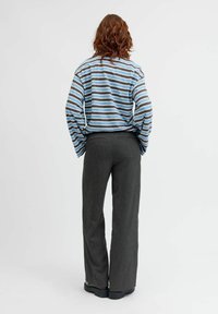 Haut rayé à manches longues en bleu, gris et blanc ; associé à un pantalon large gris foncé ; chaussures avec une semelle épaisse et plate ; vue de dos.