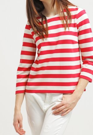 Haut à rayures rouges et blanches à manches longues avec un décolleté bateau et une coupe décontractée, associé à un pantalon blanc, mettant en valeur une texture en coton lisse.