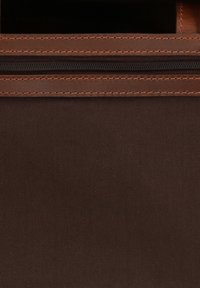 Brązowa torba z tkaniny o teksturowej powierzchni, z brązowym suwakiem i kontrastującym szwem wzdłuż górnej krawędzi. Minimalistyczny design.