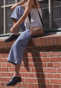 Leopardenmuster Umhängetasche mit schwarzem Riemen, weißem Ösen-Oberteil und hellblauen Jeans mit weitem Bein, ergänzt durch schwarze Schlupfschuhe.