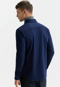 Granatowa koszula z długim rękawem o dopasowanym kroju, z szarym kołnierzykiem wewnętrznym i mankietami zapinanymi na guziki, wykonana z gładkiego materiału.