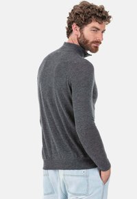 Grauer Pullover mit hohem Kragen, figurbetontem Schnitt, langen Ärmeln und geripptem Saum. Der Stoff wirkt weich mit glatter Textur.