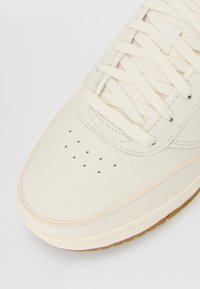 Off-white leather sneaker toe with cream laces, perforated ventilation holes, and a gum rubber sole edge on a white background.
