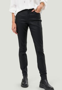 Pantalons noirs ajustés en matériau lisse et extensible. Dotés de passants de ceinture, de poches avant et de chevilles effilées, associés à des bottines noires.
