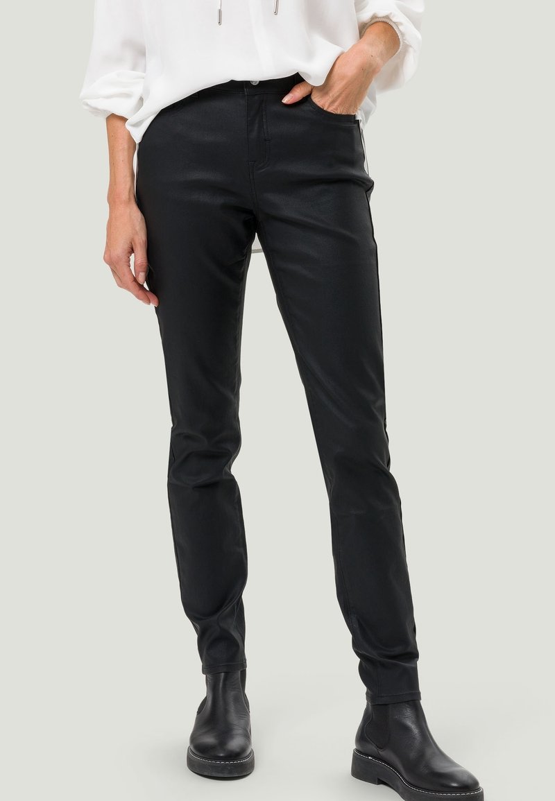Pantalons noirs ajustés en matériau lisse et extensible. Dotés de passants de ceinture, de poches avant et de chevilles effilées, associés à des bottines noires.