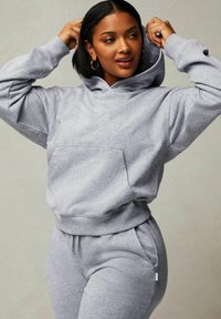 Grauer Hoodie aus weichem Stoff mit einer Vordertasche, lockerer Passform und verstellbarem Kordelzugkapuze, kombiniert mit passenden Jogginghosen.