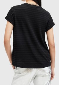 Camiseta negra con mangas cortas enrolladas, con una sutil textura de rayas horizontales, combinada con pantalones metálicos plateados.