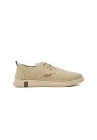 Zapatillas de lona beige con una textura suave, forma redondeada, diseño de cordones y acentos marrones, que presentan un logotipo y una cinta en el talón.