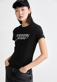 Svart bomulls t-skjorte med hvit "tommy jeans" logo. Har korte ermer og rund hals. Kombinert med mørkegrå jeans.