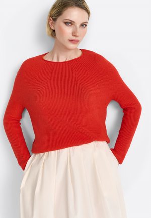Red knitted sweater with ribbed texture, round neckline, and long sleeves, paired with a cream-colored skirt featuring pleats.