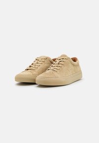 Beige nubuk-tossut kengät, joissa on tekstuuripinta, nauhakiinnitys ja sileä kumipohja. Pyöreä kärki ja minimalistinen muotoilu.