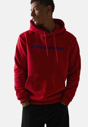 Czerwony bawełniany hoodie z kieszenią z przodu i kapturem na sznurku. Posiada niebieski wyszywany tekst "diverse" na klatce piersiowej. Gładka tekstura.