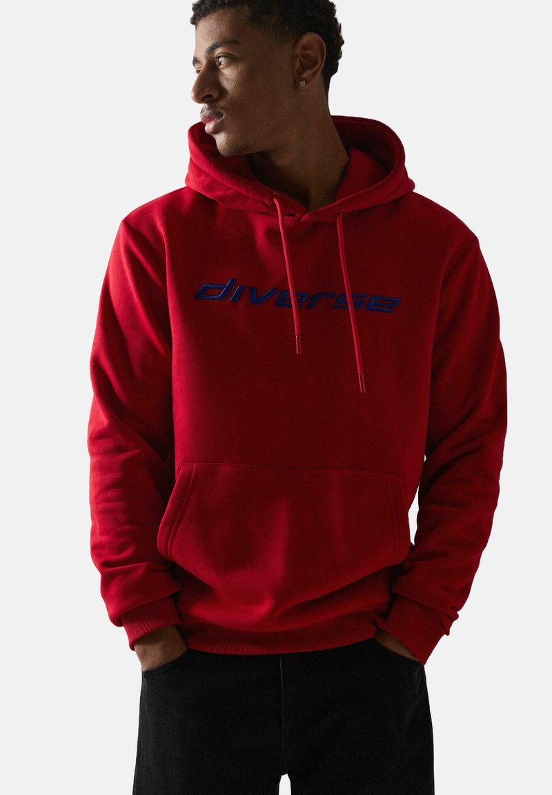 Czerwony bawełniany hoodie z kieszenią z przodu i kapturem na sznurku. Posiada niebieski wyszywany tekst "diverse" na klatce piersiowej. Gładka tekstura.