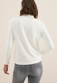 Sweat-shirt blanc avec une texture mouchet�ée et des manches longues, doté d'un col haut et d'une coupe décontractée. Porté avec un jean gris.