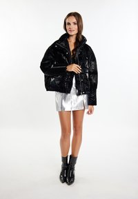 Giacca puffer nera lucida con colletto alto e bottoni frontali, abbinata a una mini gonna argento metallico e stivaletti neri a punta.