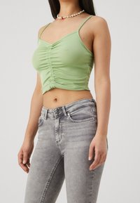 Top cropped verde claro con un diseño fruncido en la parte delantera y tirantes finos, combinado con jeans de tiro alto gris claro que cuentan con bolsillos estándar.