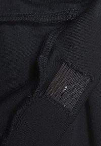 Svart tyg med fin struktur som har en inre etikett och detalj med sömnad. Tyget verkar elastiskt och är designat för användning i kläder.
