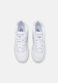 Paire de baskets blanches New Balance 550 vues de dessus sur un fond clair uni avec lacets et logo visibles.