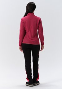 Fleecejacke in Pink mit hohem Kragen, kombiniert mit schwarzen Hosen mit pinken Seitenstreifen. Strukturierter Stoff und taillierte Passform.